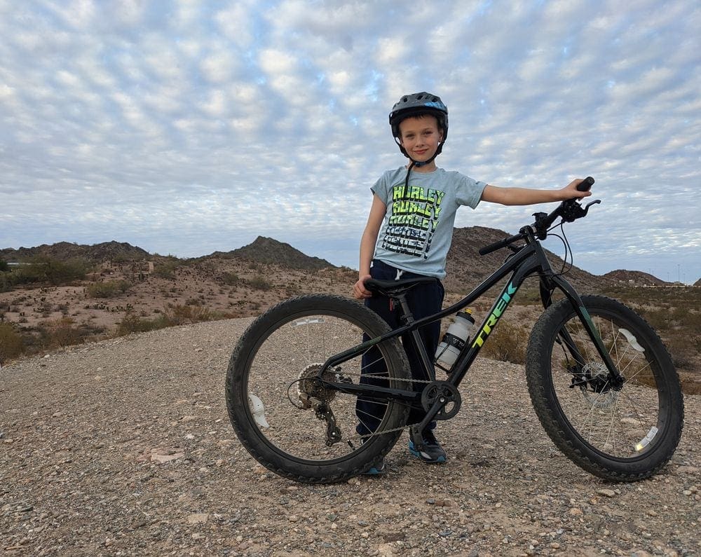 A young boy wearing a helment poses with his bicycle on a trail at Dreamy Draw Loop, one of the best places to visit on a Phoenix itinerary for families.