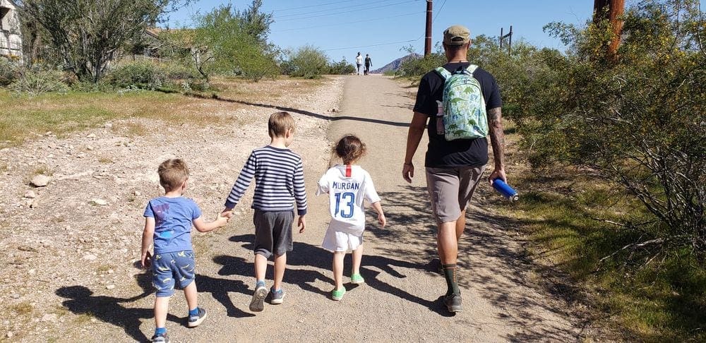 A dad and his three kids hike along a desert trail in Phoenix, one of the best affordable spring break destinations for families. 