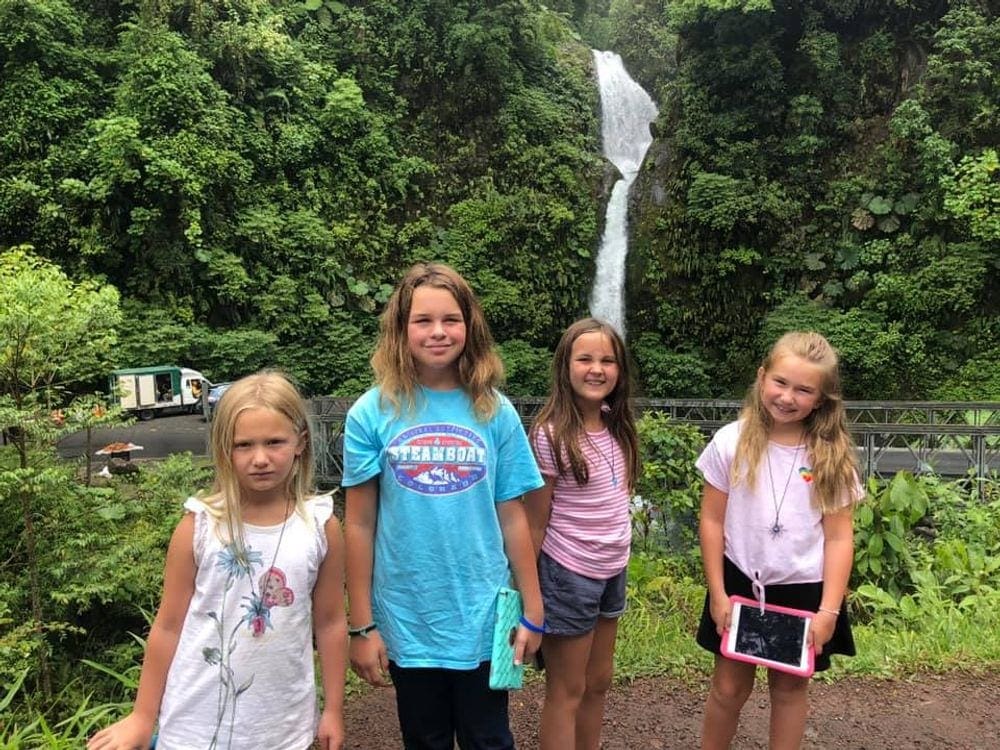 Four kids stand smiling in front of La Paz Waterfall in Costa Rica.