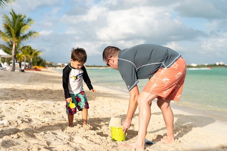 A dad and his young son play on the beach with sand toys in Turks & Caicos, one of the best hot places to visit in December for families.