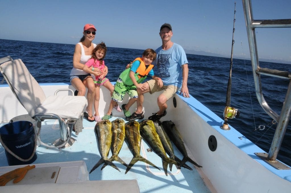 A family of four sits at the edge of a boat with their large catch of fish in Costa Rica.