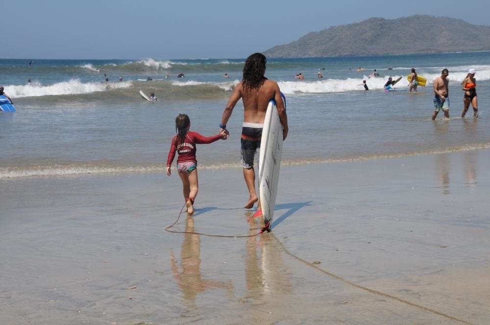A young girl holds the hand of a surf instructor while walking toward the water in Costa Rica.