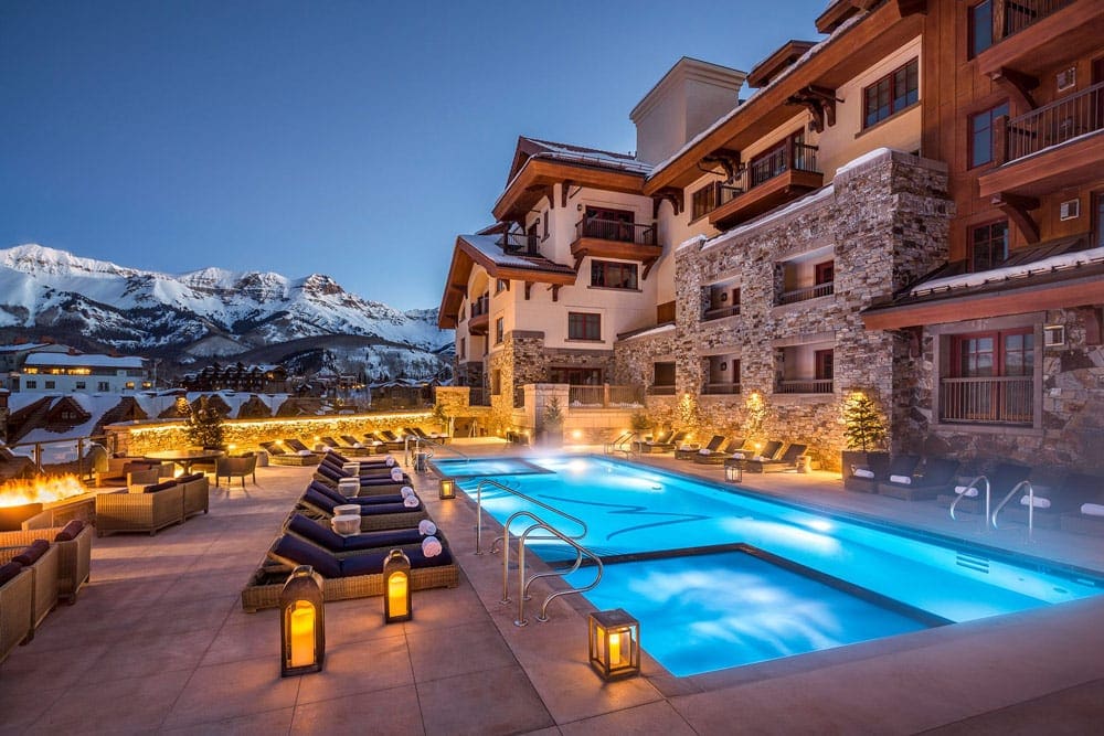 The outdoor pool at Madeline Hotel & Residences, Auberge Resorts Collection, one of the best ski-in/ski-out resorts in the U.S. for families, nestled between lounge chairs and the restor buildings at night.