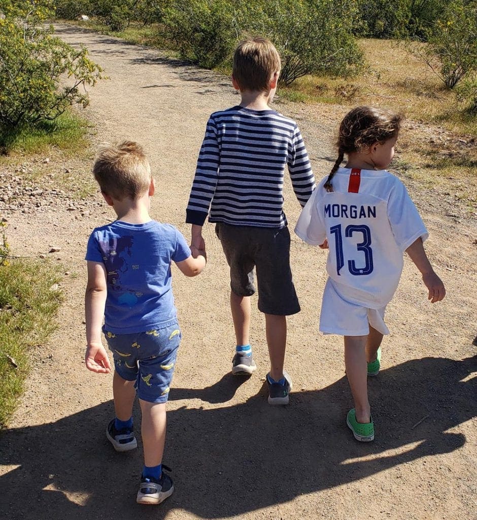 Three kids, holding hands, walk along a hiking path at Papgo Park in Phoenix.