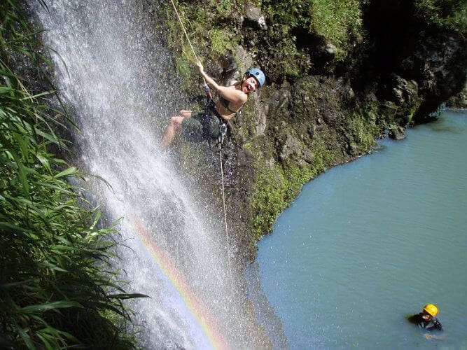 A young girl rappels down a waterfall with a rainbow going through it.