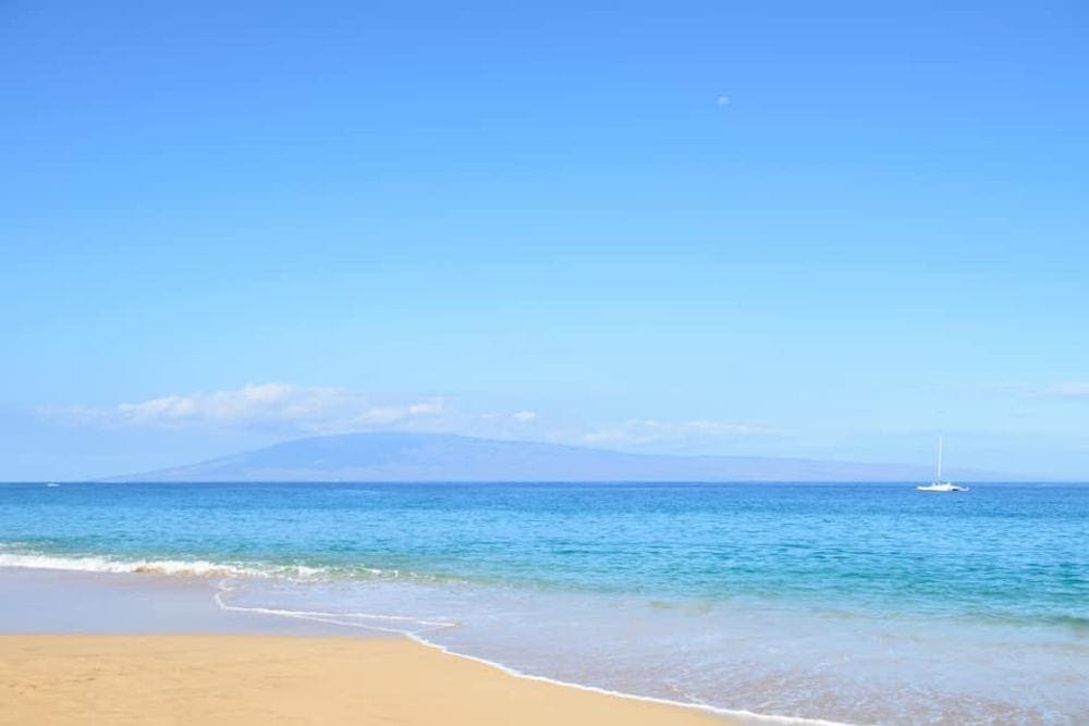 A clear day at the Kaanapali Beach, with sand in the foreground and bright blue water in the background.