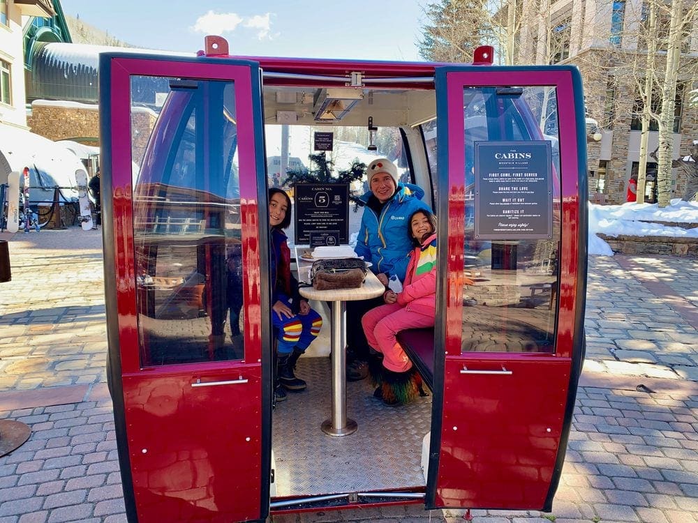 Two kids and their dad smile from inside a stationary gondola at Telluride.