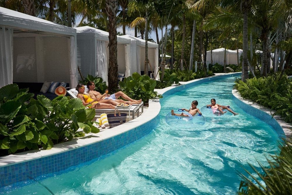 Two kids float past their resting parents while enjoying the lazy river on a sunny day at Tidal Cove.