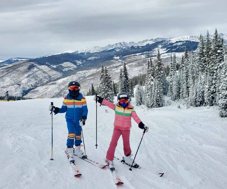 Two kids, one in a blue ski suit and one in pink, ski along the runs at Vail Ski Resort.
