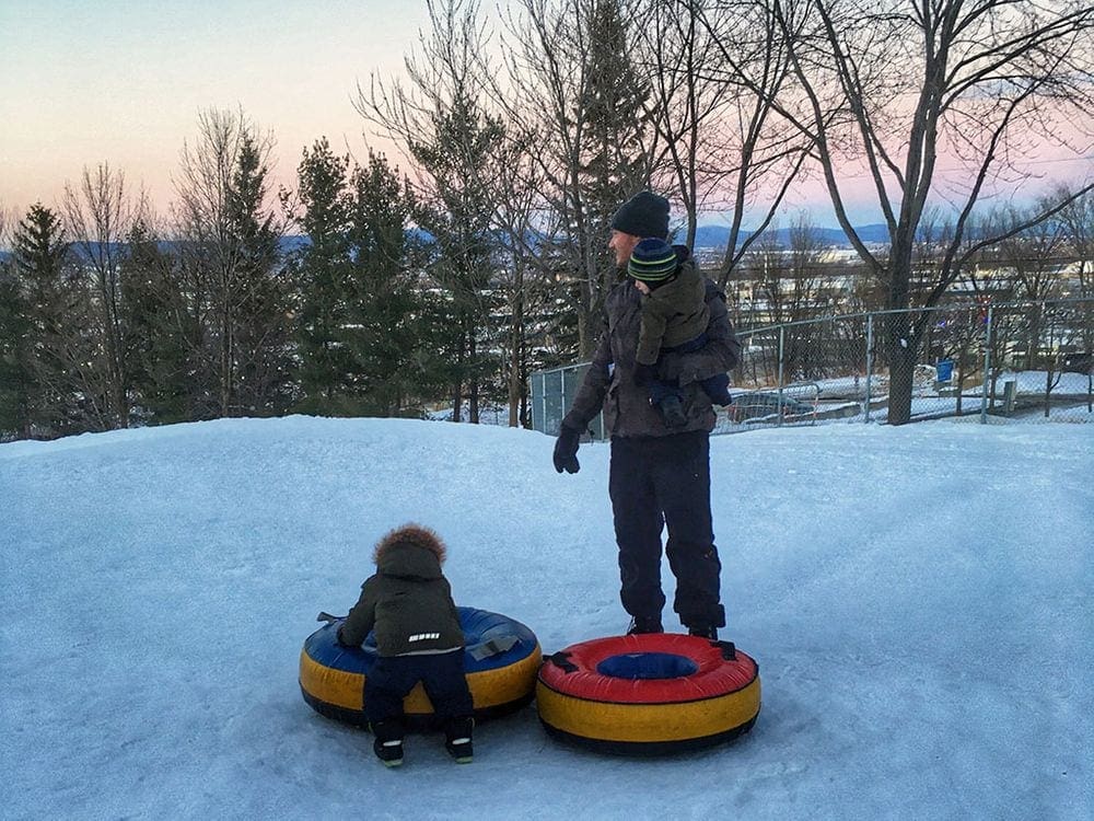 A dad and his two young kids play with snowtubes in Montreal, one of the best things to do during your three-day Montreal itinerary with kids.