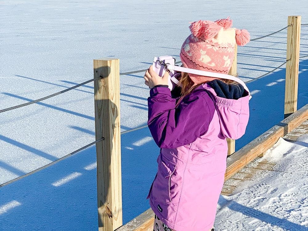 A young girl holds a camera up to her face on a snowy day.