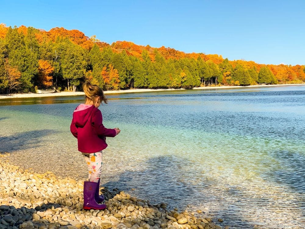 A young girl stands on School House Beach in Door County on a beautiful fall day, a great stop for a Midwest road trip with kids.