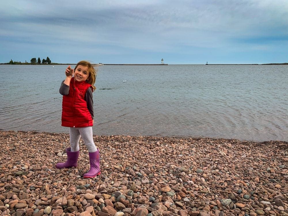 Little girl on a pebble beach of Lake Superior in Grand Marais, Minnesota, a great stop for a Midwest road trip with kids.