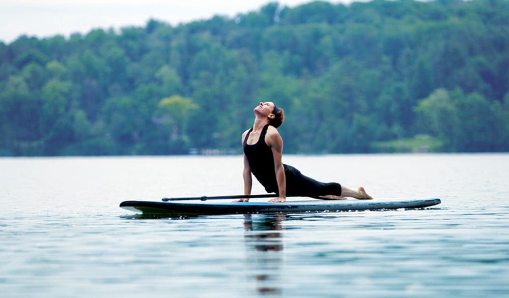 A woman does a yoga position on a paddle board while on a mom's weekend getaway.