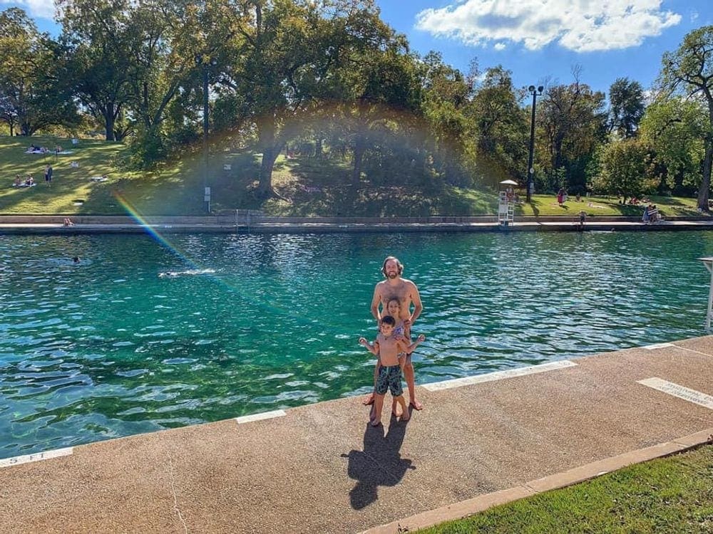 A dad and his two kids stand in front of the water at the Barton Springs Pool.