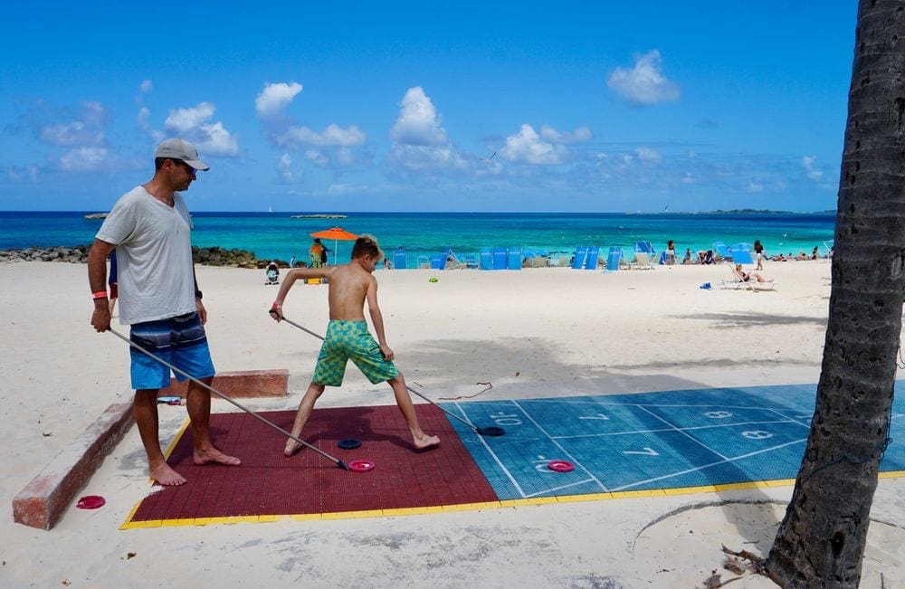 A dad and his sone play shuffel board on the beach.