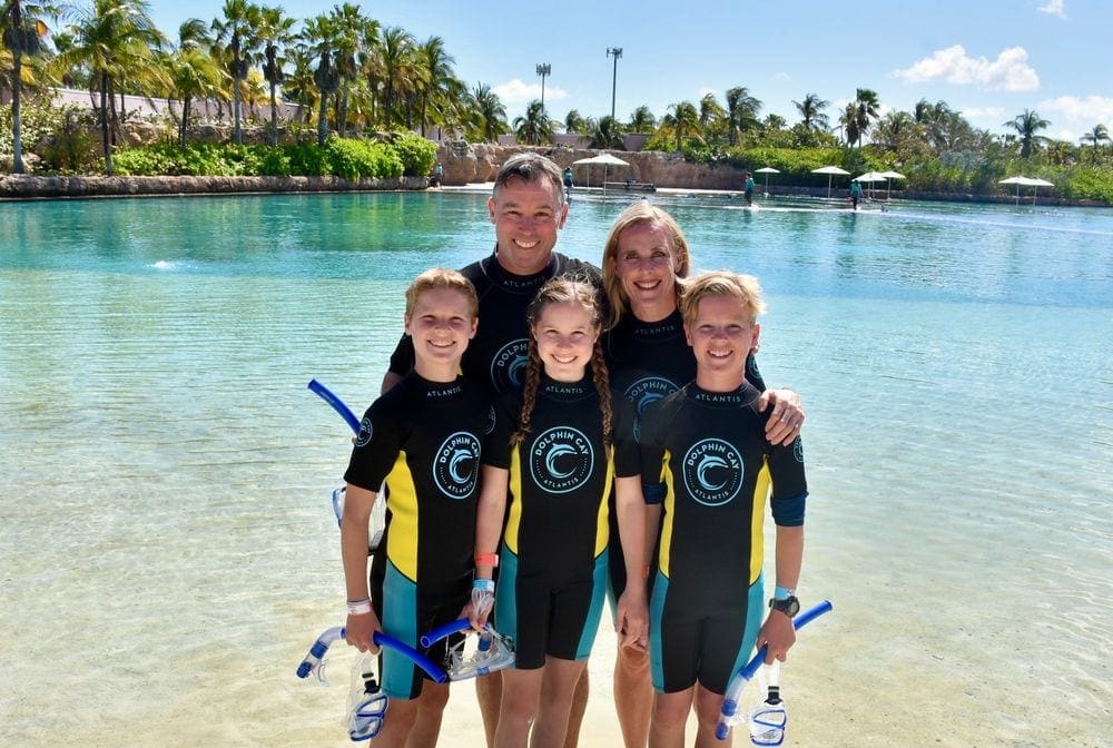 A family of five stands smiling in snorkel gear.
