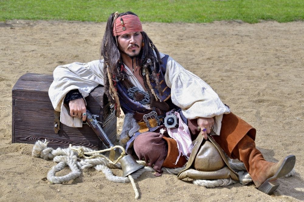 Johnny Depp in costume as a pirate leaning on a treasure chest.