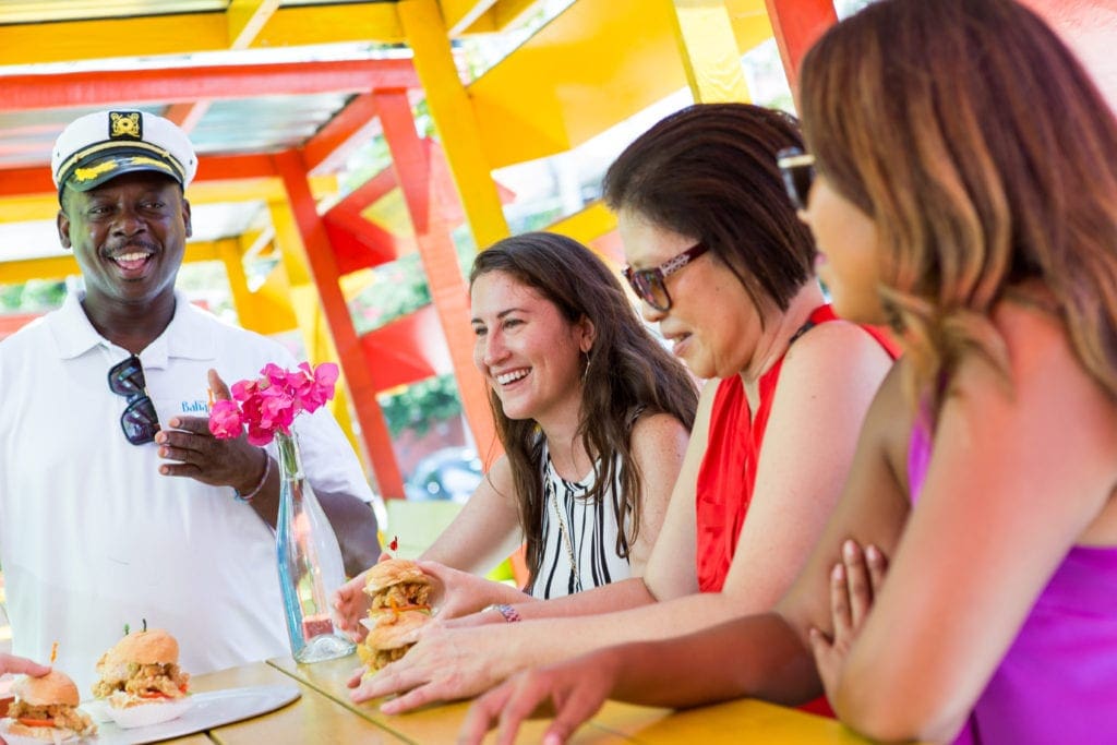 Three girls tasting food served to them by a food tour guide.