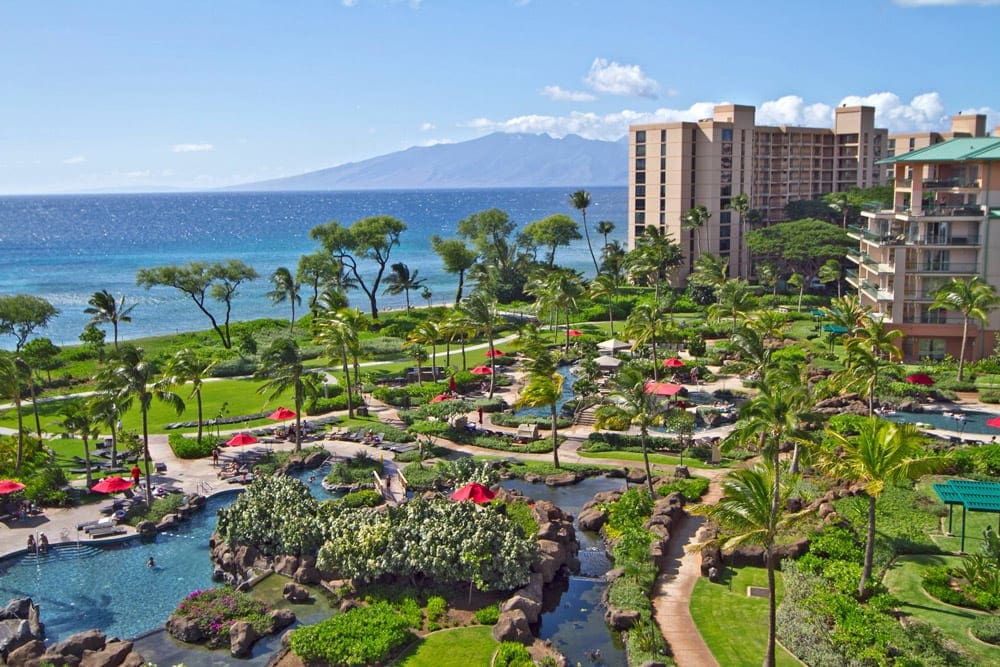 An aerial view of the Honua Kai Resort & Spa, featuring several pools, green lawns, and tall resort buildings.