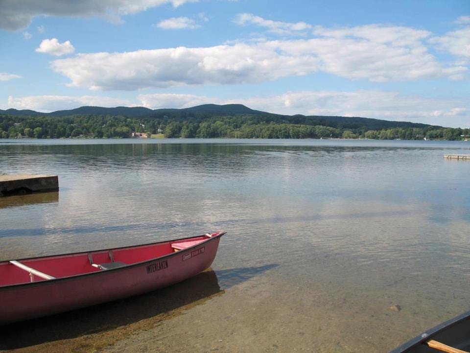 A red canoe rests on the water near a dock along the lakeshore of Interlaken Inn, one of the best hotels in Connecticut for families.