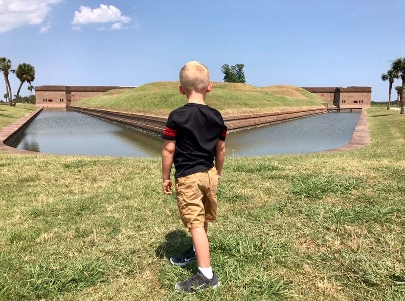 A young boy explores Old Fort Jackson on a sunny day while looking at the moat around the buildings.