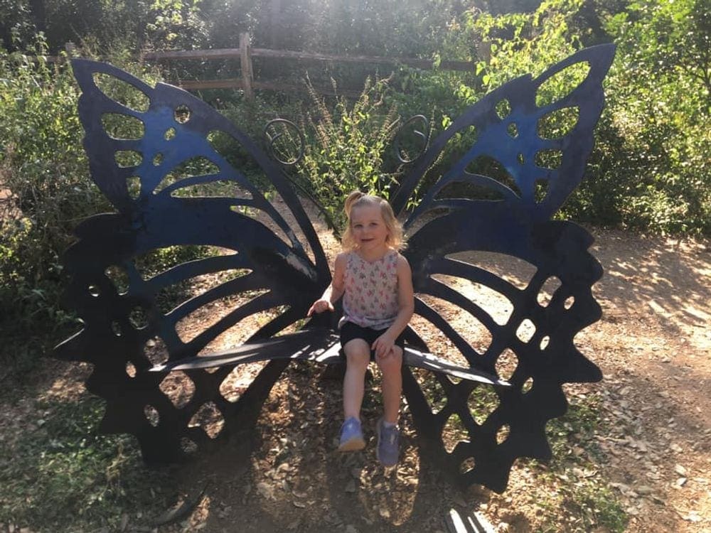 A young girl sits on a butterfly bench at the Botanical Garden in Austin.