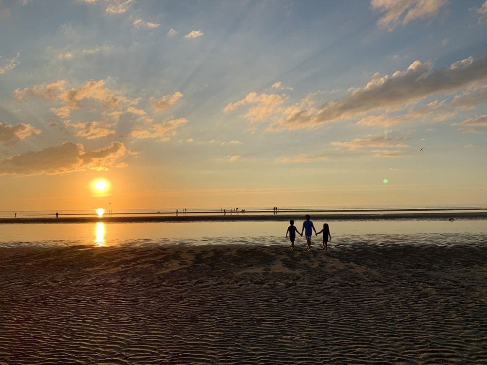 A mom holds her children's hand while walking on a beach in Cape Cod at sunset, one of the best weekend getaways near Boston for families.