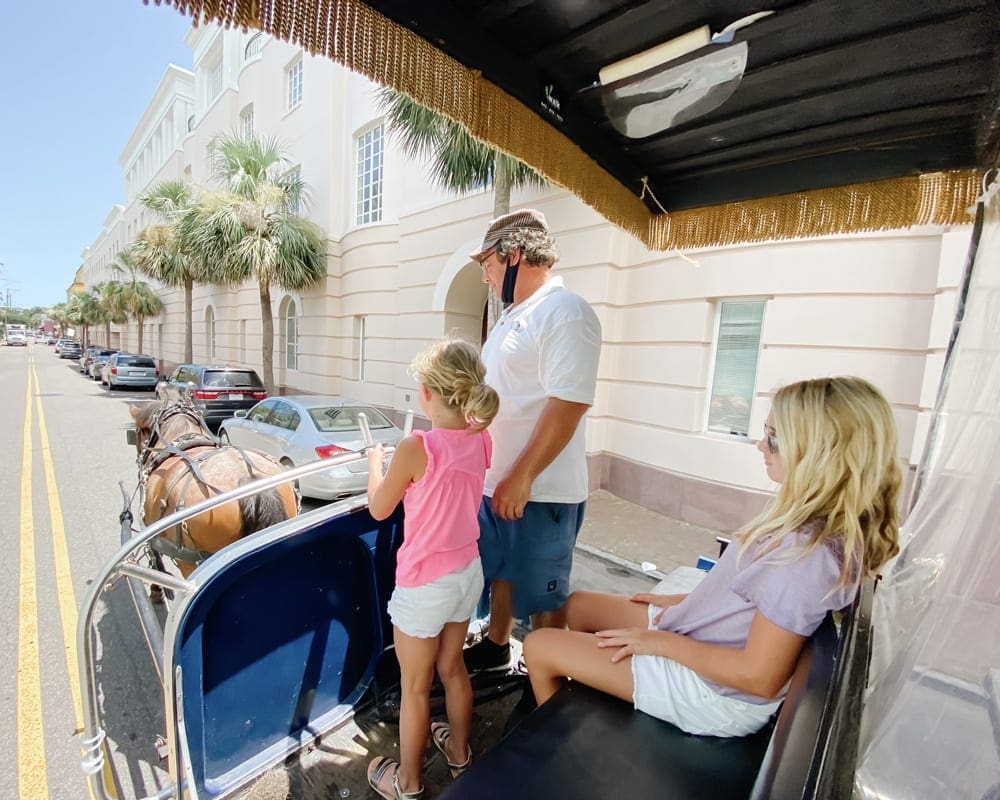 A family of three rides in a horse-drawn carriage in Charleston, one of the best things to do with kids in Charleston.