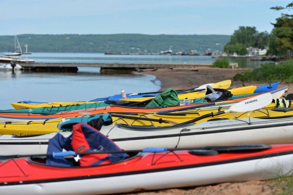 A series of colorful kayak rest on a beach on Madeline Island on Lake Superior, one of the best places to rent a lake house in Wisconsin.