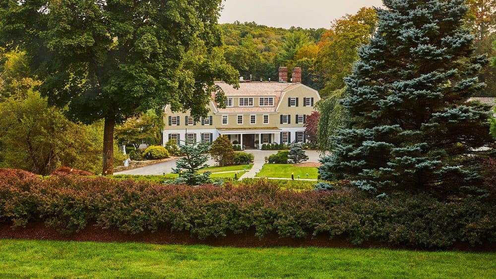 The main building for the Mayflower Inn & Spa, Auberge Resorts Collection within a beautiful natural surround, including lush trees and foliage.