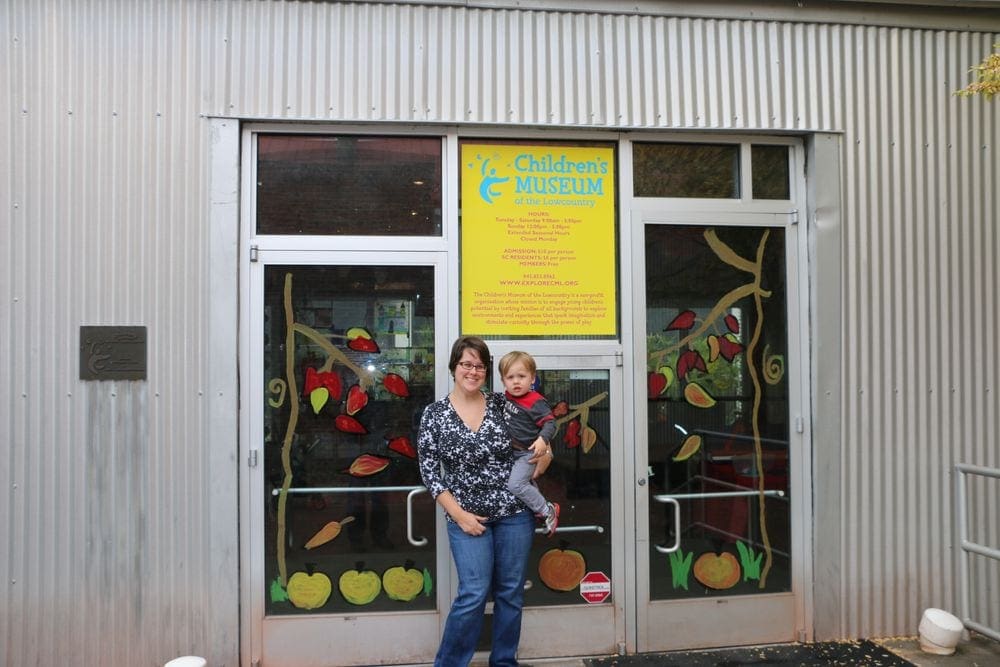 A mom holds her toddler in front of the Children's Museum in Charleston, one of the best places to stop on an NYC to Miami itinerary for families!