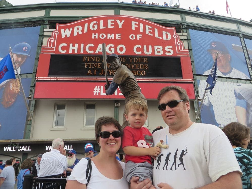 A family of three stands in front of the iconic Wrigley Field sign, one of the best kids activities in Chicago.