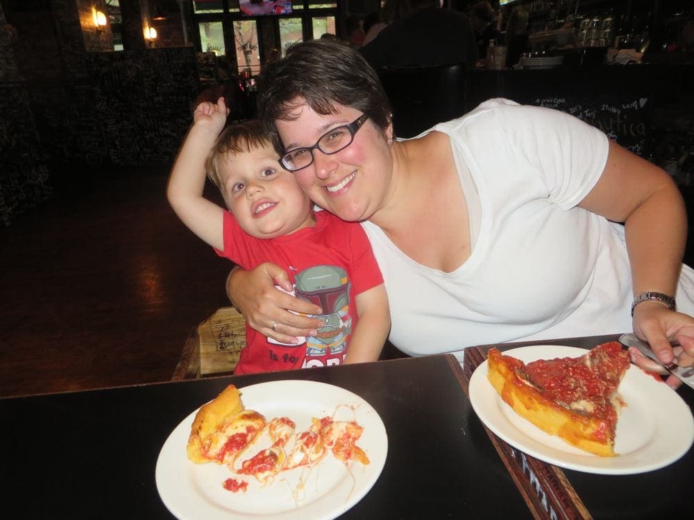 A young boy and his mom smile while enjoying deep dish pizza in Chicago.