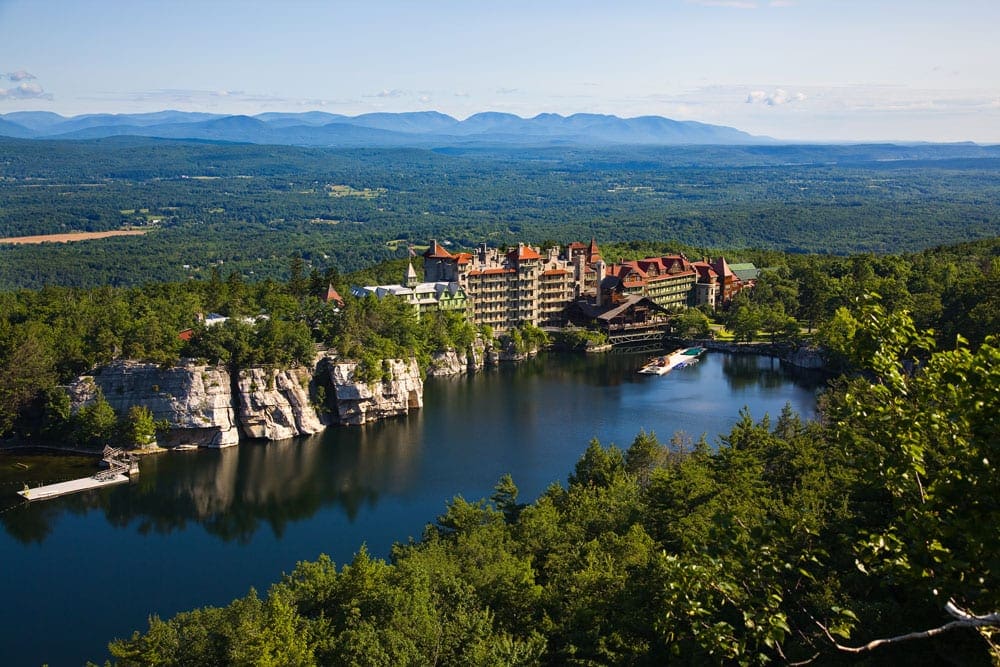 An aerial view of the grounds of Mohonk Mountain House, neastled along a body of water on a summer day.