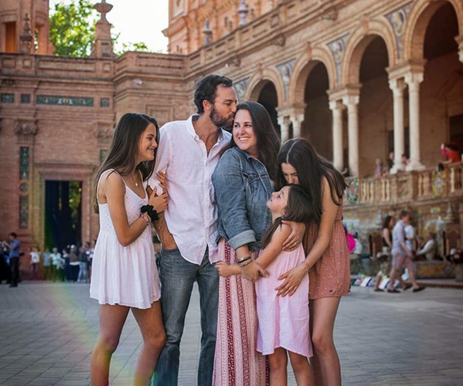 A family of give hugs while enjoy a sunny day in a Spanish plaza.