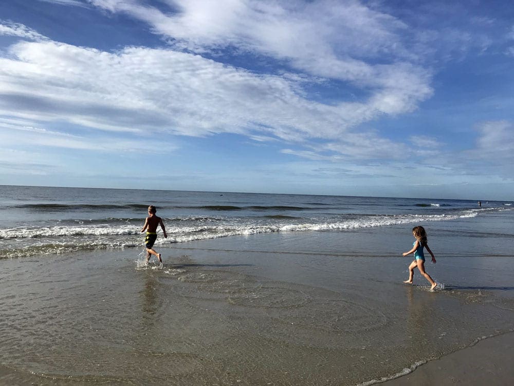 Two kids splash in the water at a beach in Hilton Head on a sunny day.