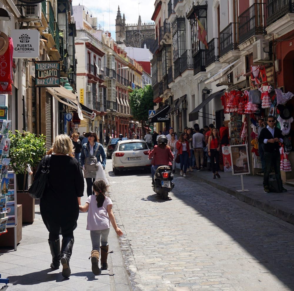 A mom and child walk down a street of Seville hand in hand.