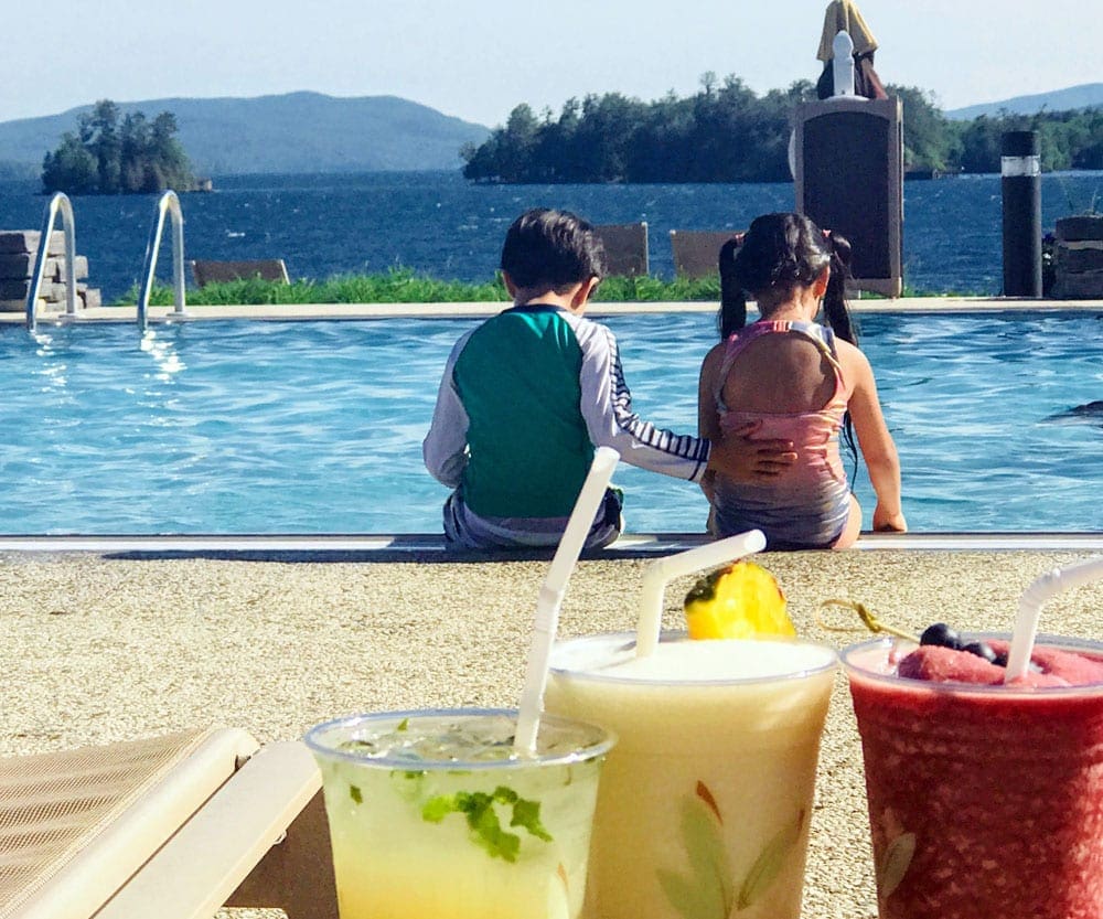 Two kids sit at the edge of a pool at The Sagamore, while their fruity drinks wait for them at the lounger.