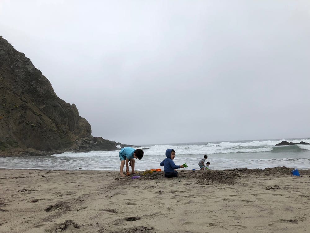 Three kids play in the sand on a beach near Big Sur, one of the best places to visit in California with kids. 