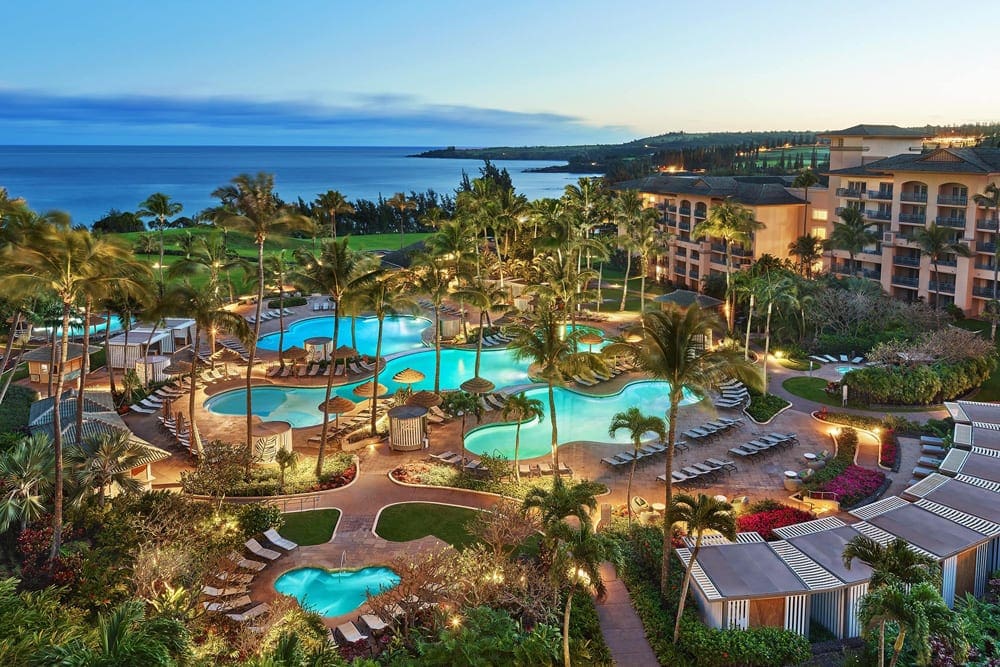 An aerial view of The Ritz-Carlton, Kapalua at night, featuring well-lit paths, buildings, and pool area.