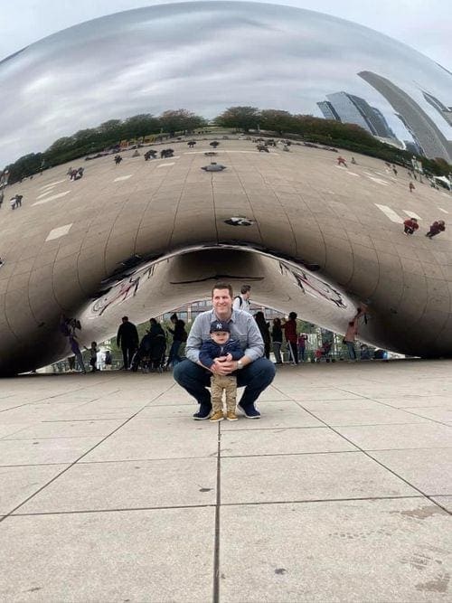 A dad crouches with his toddler son in front of "the Bean", one of the best kids activities in Chicago.