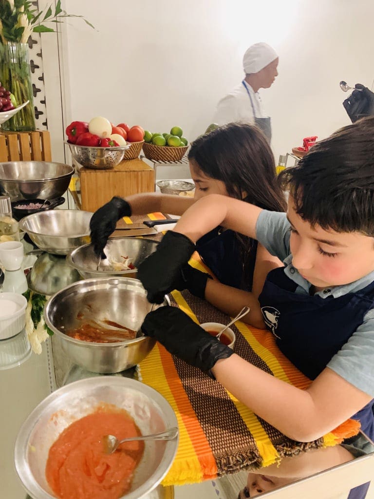 Two kids wearing black kitchen gloves mix spices by hand while taking a cooking class, one of the best things to do in Cartagena with kids.