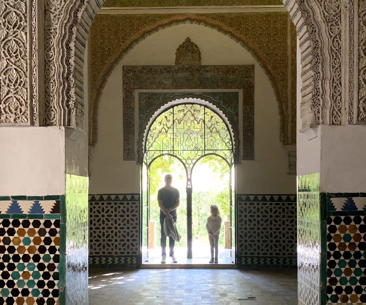 Two people stand in a doorway at the end of a long, decorated hallway in Seville.