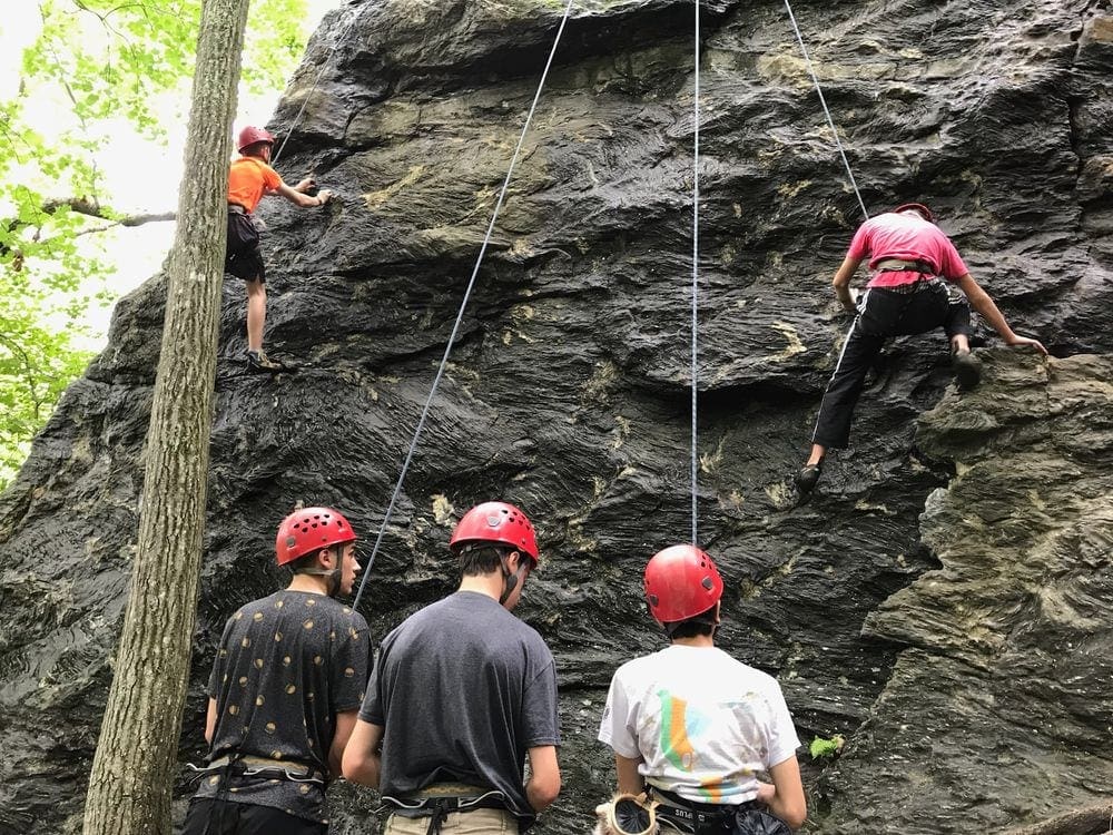 Two people rappel down a cliffside inside Acadia National Park, while three other climbers look on.