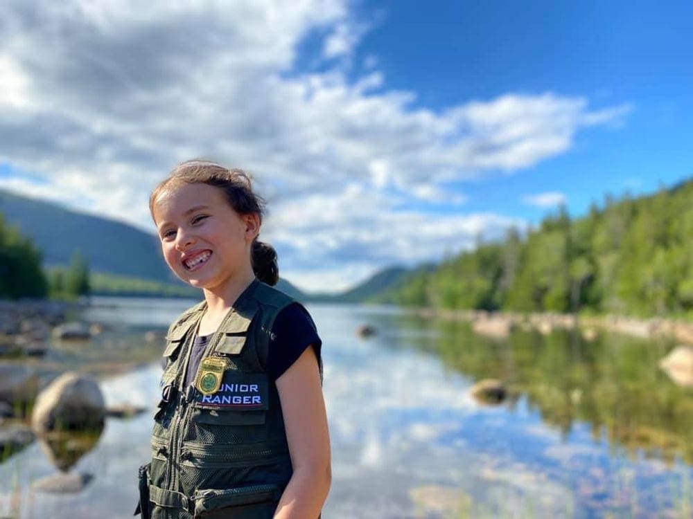 A young girl smiles broadly on a sunny day while explore Jordan's Pond in Acadia National Park.