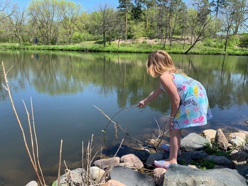 A young girl pokes a stick in the water on a sunny day in Northfield, one of the best places to explore near the Twin Cities with kids.