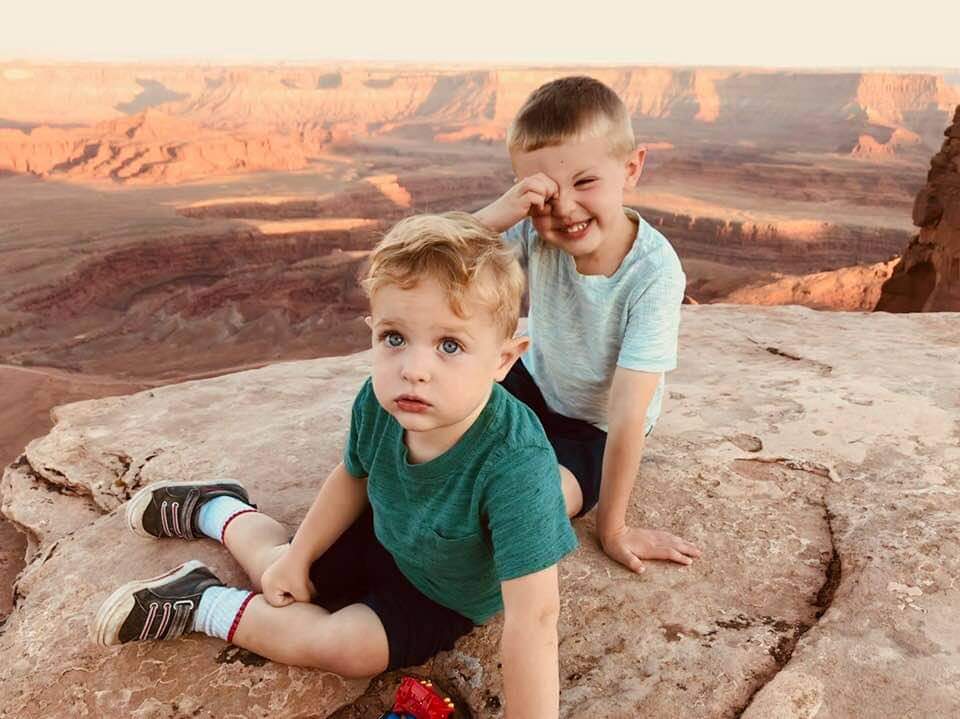 Two kids sit together along a rock ledge within Dead Horse Point State Park, one of the best things to do in Moab with kids.