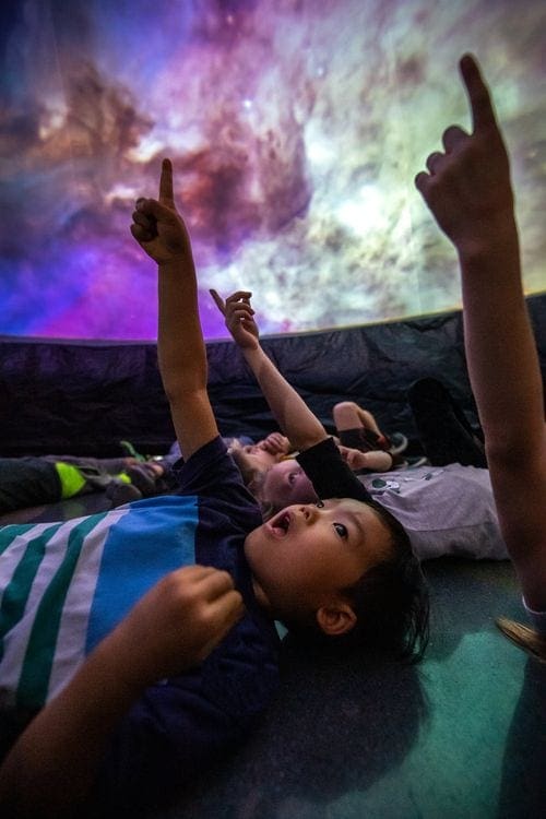 Kids excitedly point up as they enjoy a show at the Bell Museum planetarium.
