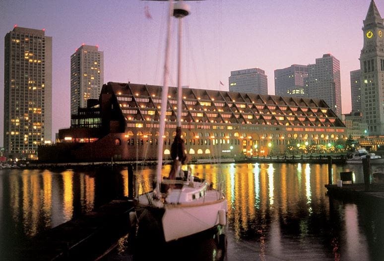 A view of the Boston Marriott Long Wharf from across the water, with a ship on the water at night,